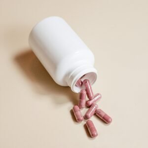 A white bottle of pink capsules spills onto a beige background, perfect for healthcare themes.