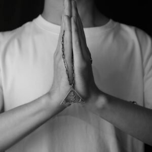 Black and white image of clasped hands in prayer with a triangle pendant.
