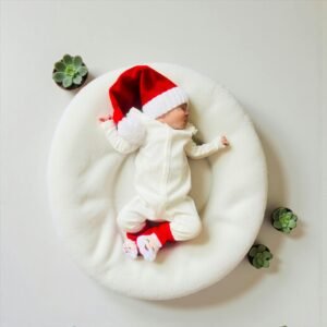 Cute newborn baby wearing a Santa hat sleeping on a cozy white cushion with succulents around.