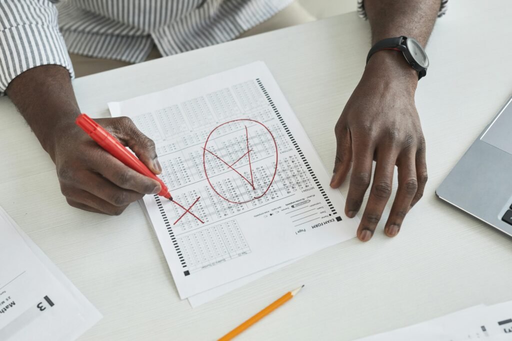 Close-up of a teacher marking a test paper with a red marker on a desk.